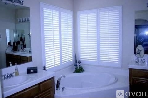 A bathroom with a tub, sink, and window with blinds.