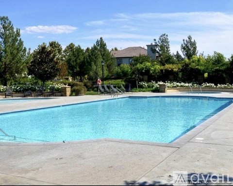 A large swimming pool surrounded by a concrete patio and a residential house in the background.