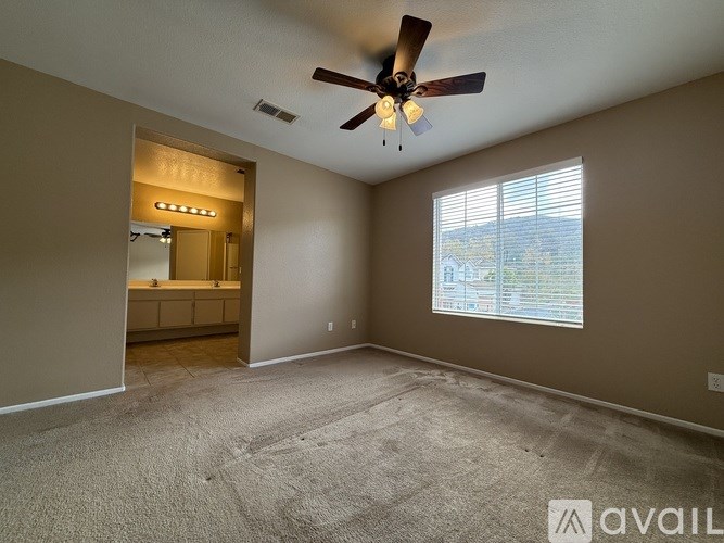 A spacious room with a ceiling fan and a window with blinds.