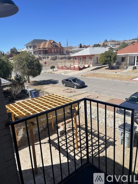 A balcony with a table and chairs overlooks a street with cars and houses.