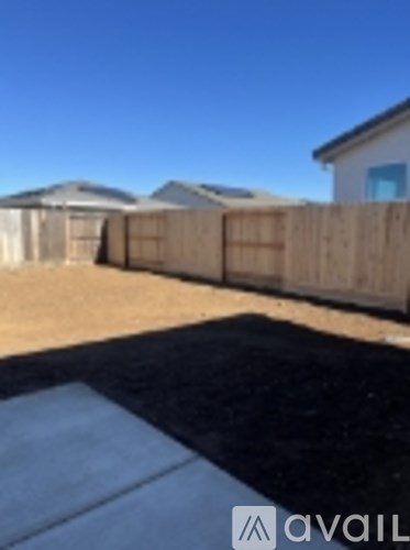 A backyard with a wooden fence and a black tarp on the ground.