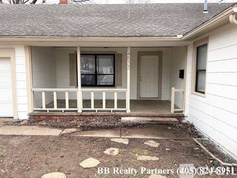 A white house with a porch and a BB Realty Partners sign in the front yard.