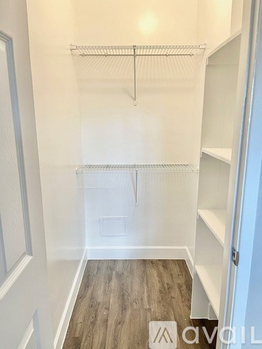 A white walk-in closet with a wooden floor and white shelves.