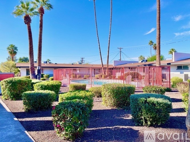 A red building with a pool in front surrounded by green bushes and palm trees.