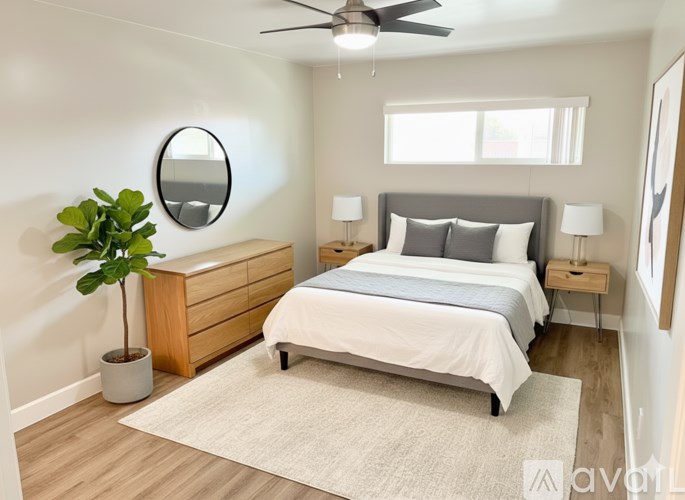 A bedroom with a bed, nightstand, and a plant.