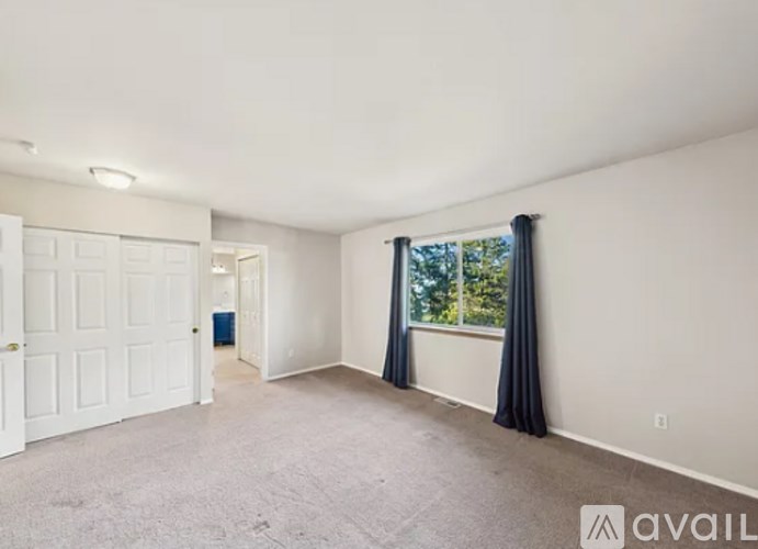 A spacious room with a carpeted floor, a window with black curtains, and a door on the left.