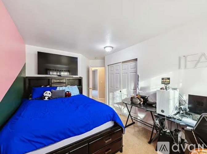 A bedroom with a bed, desk, and computer setup.