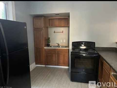 A kitchen with a black fridge, black stove, and wooden cabinets.