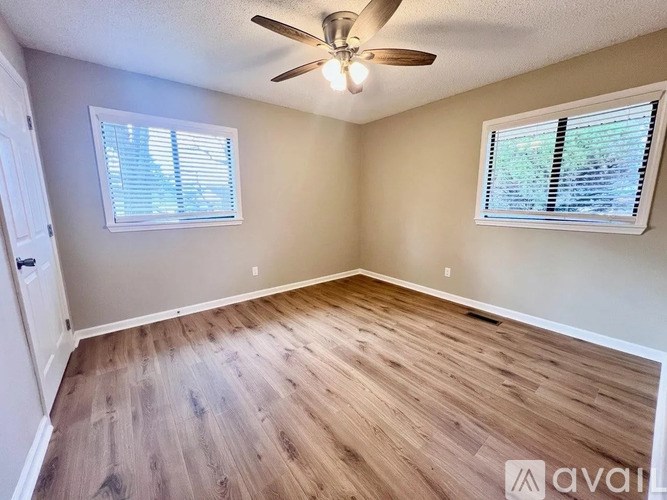 A room with a ceiling fan and two windows.