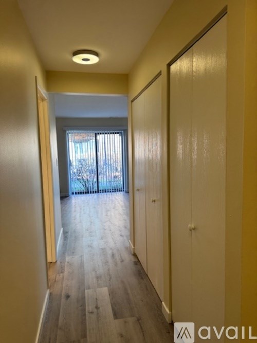A hallway with wooden floors and white walls leading to a glass door.