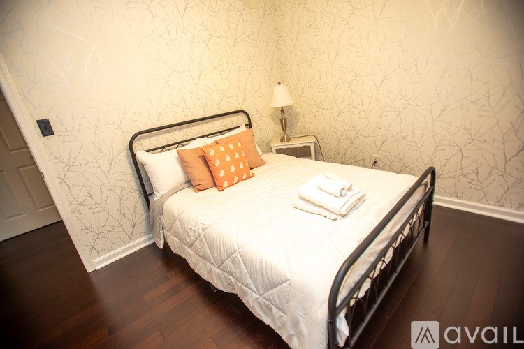 A bed with a white comforter and an orange pillow is in a room with a lamp on a nightstand.