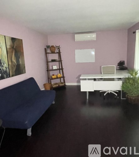 A living room with a blue couch, a white desk, and a painting on the wall.