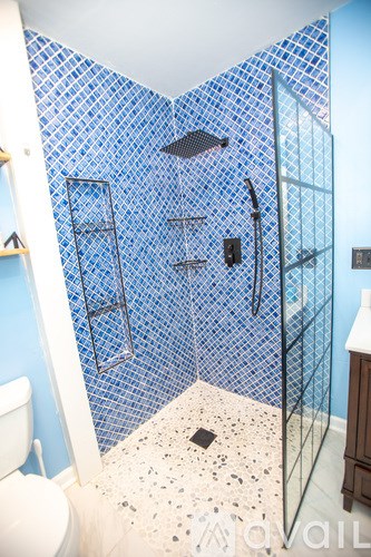 A bathroom with a blue tiled shower and a white toilet.