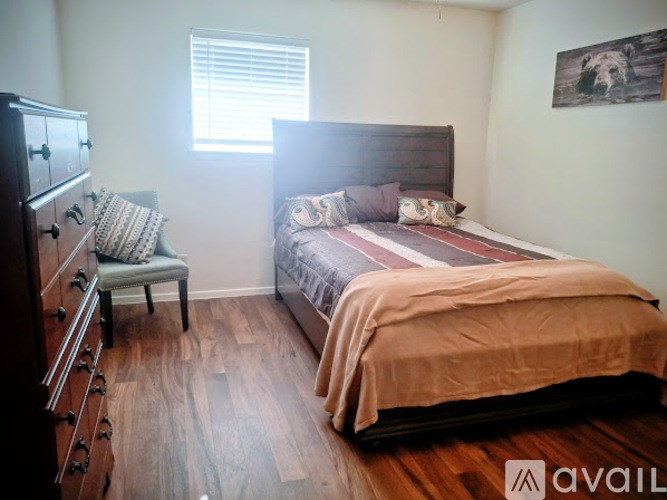 A bedroom with a bed, chair, and wooden floor.
