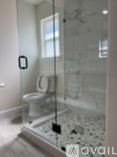 A bathroom with a glass shower stall and a toilet.