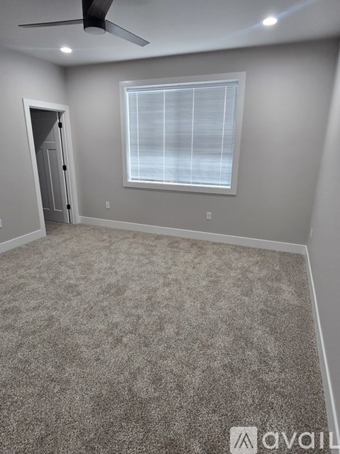 A room with a carpeted floor, a window with blinds, and a ceiling fan.