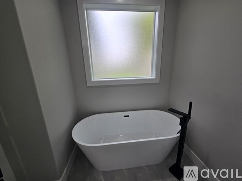 A white bathtub sits under a window in a bathroom.