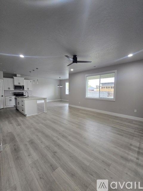 A spacious living room with a kitchen area and a ceiling fan.