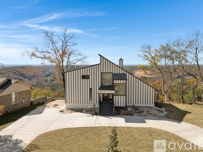 A modern house with a sloped roof and a balcony is surrounded by a grassy area and trees.