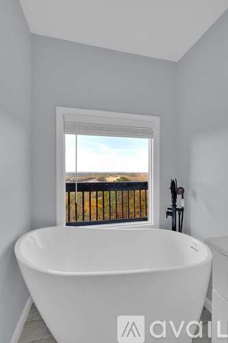 A white bathtub is in a bathroom with a window overlooking a fence.