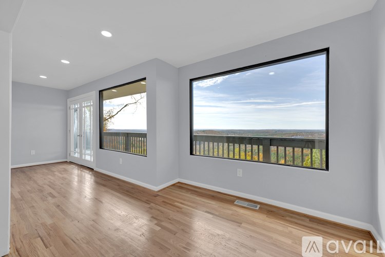 A spacious room with wooden floors and a large window with a view of the sky.