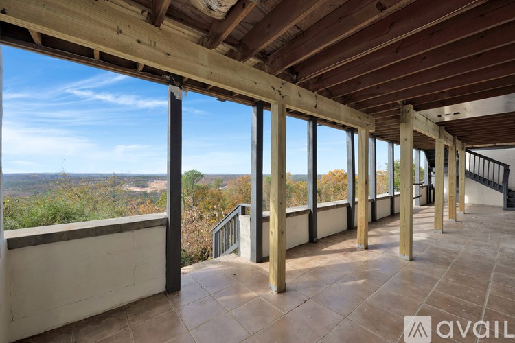 A balcony with wooden pillars and a tiled floor overlooks a scenic view.