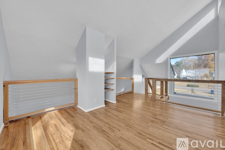 A room with wooden floors and white walls, with a window that shows a view of a street.