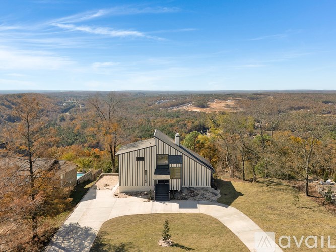A modern house with a grey exterior is surrounded by trees in a rural setting.