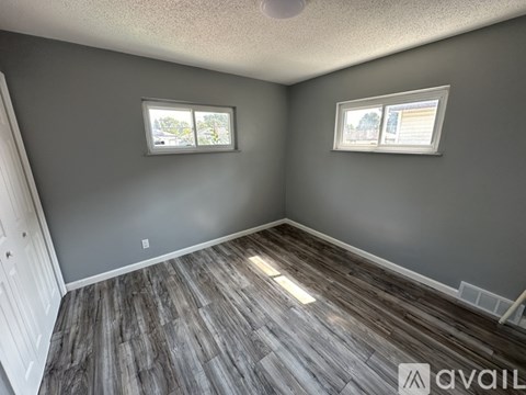 A room with grey walls and wooden flooring with two windows.