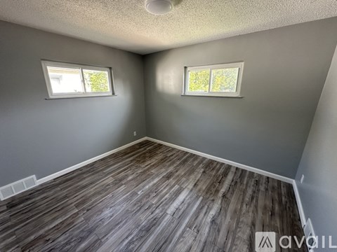 A room with wooden flooring and two windows.