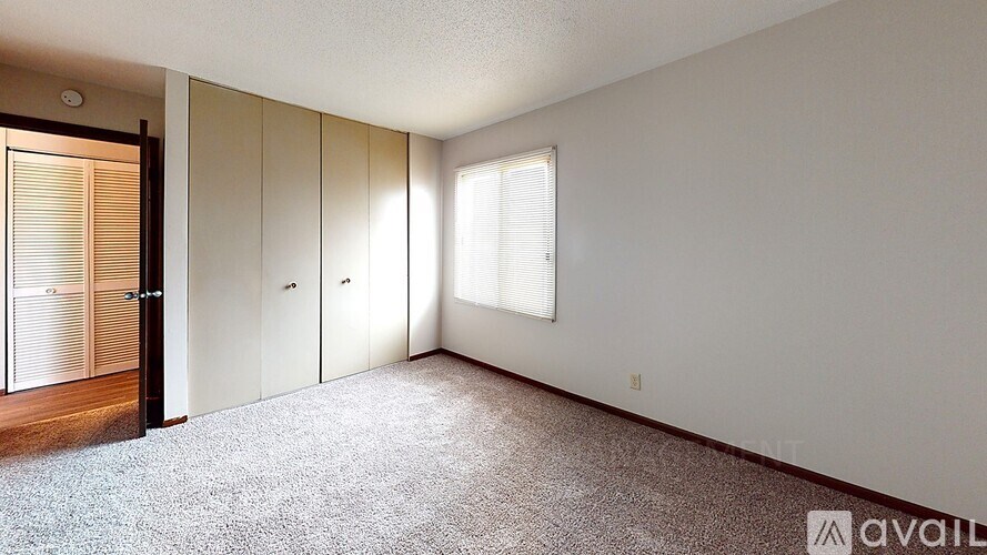 A room with a carpeted floor, a door, and a window with blinds.