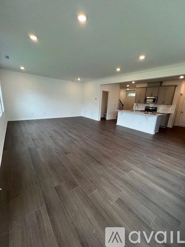 A spacious room with wooden flooring and a kitchen area in the background.