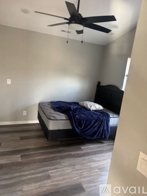 A bedroom with a bed covered in a blue blanket and a ceiling fan.
