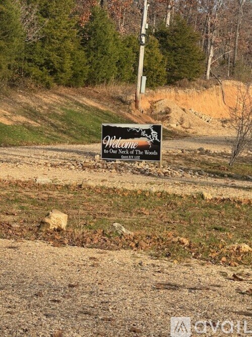 A sign that says "What's new at the woods" is in front of a wooded area.
