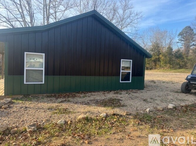 A black and green building with two windows sits in a field.