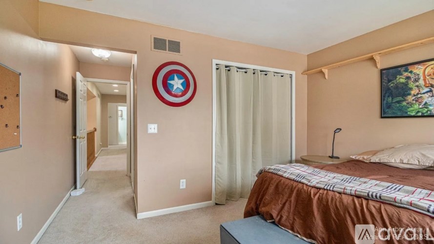 A bedroom with a bed, a window with curtains, and a Captain America shield on the wall.