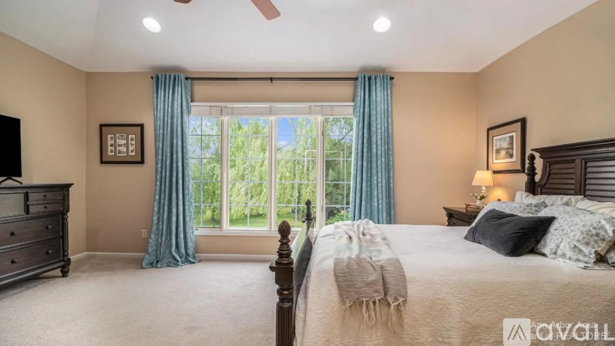 A bedroom with a large bed, a dresser, and a window with blue curtains.