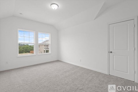 A spacious room with a carpeted floor, a door, and a window showing a view of a building and trees outside.