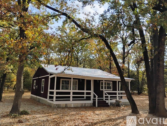 A small house with a porch is surrounded by trees with yellow leaves.