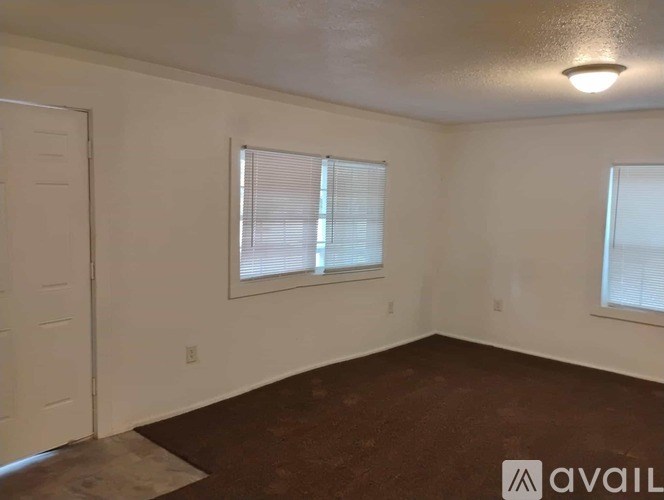 A room with brown carpet and two windows with blinds.