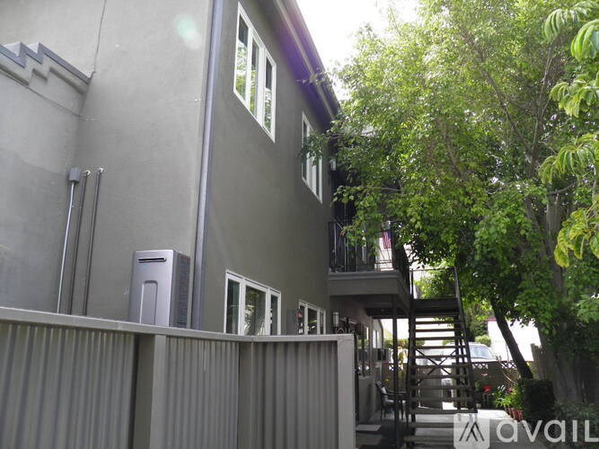 A grey building with a balcony and a tree in front.
