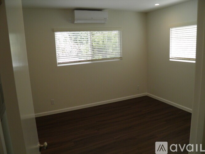 A room with wooden floors and two windows with blinds.