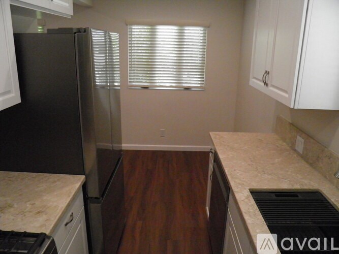 A kitchen with a black refrigerator, white cabinets, and a marble countertop.