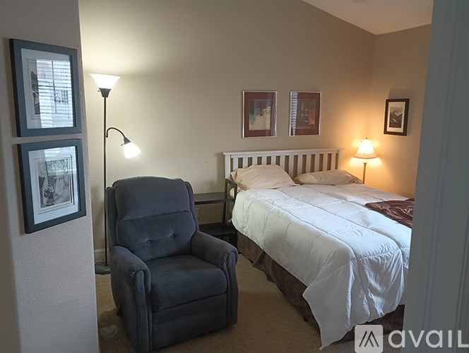 A bedroom with a bed, chair, and two pictures on the wall.