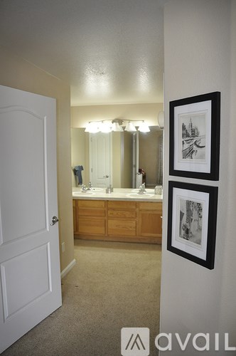 A bathroom with a white door, a vanity with a mirror and lights, and two pictures on the wall.