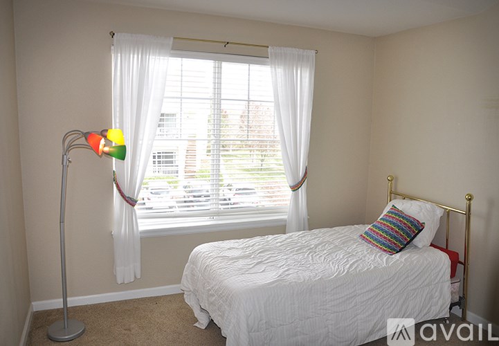 A bedroom with a white bed and a floor lamp with a multicolored shade.