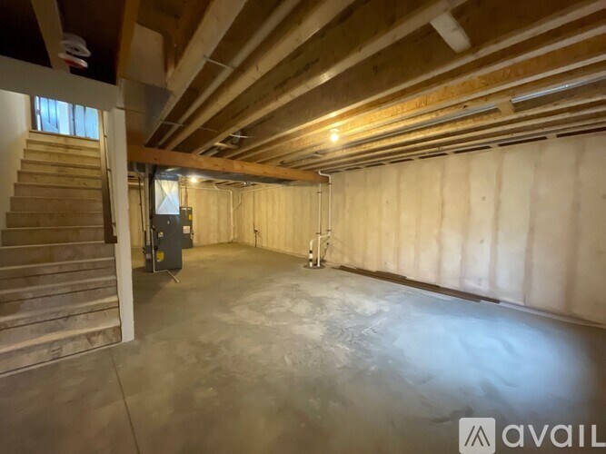 A spacious attic room with wooden beams and a staircase on the left side.