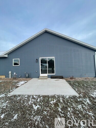 A house with a grey siding and a white door is surrounded by a gravel path.