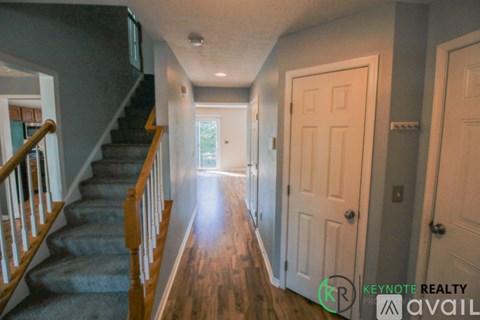 A hallway with a staircase on the left and a door on the right.