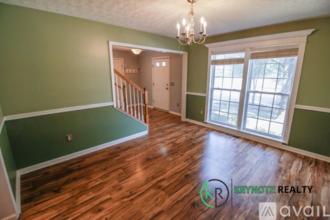 A room with green walls and wooden floors, with a chandelier and a window.